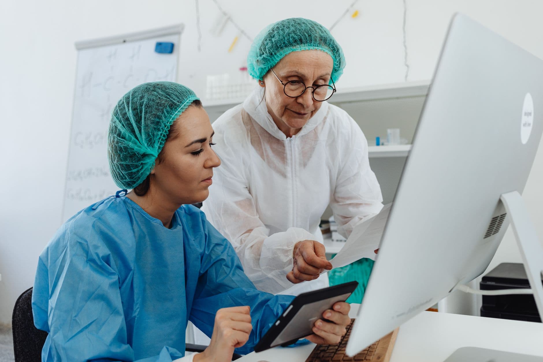Two pharmacy professionals in protective gowns reviewing an operational report together